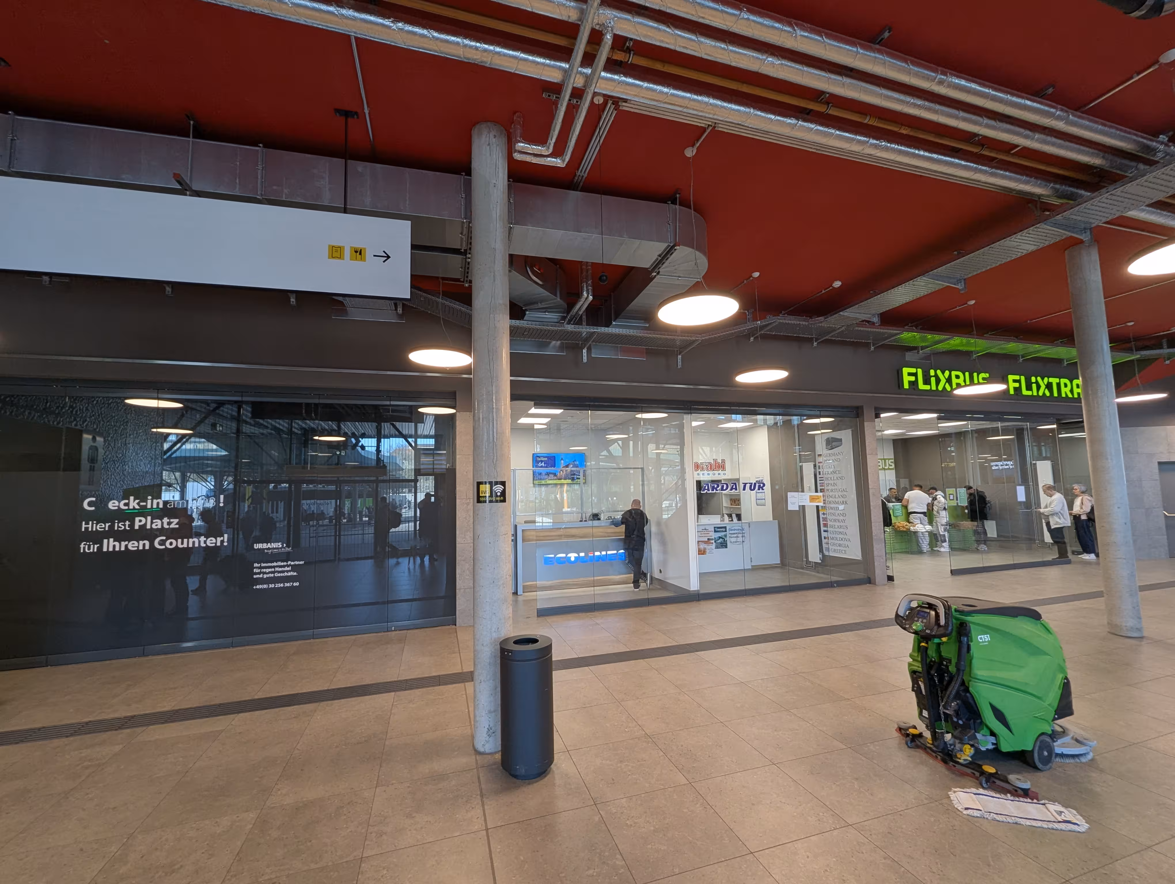 Eine Innenansicht der Wartehalle, im Hintergrund befinden sichzwei Schalter, im Vordergrund steht ein Mülleimer und etwas Reinigungsgerät